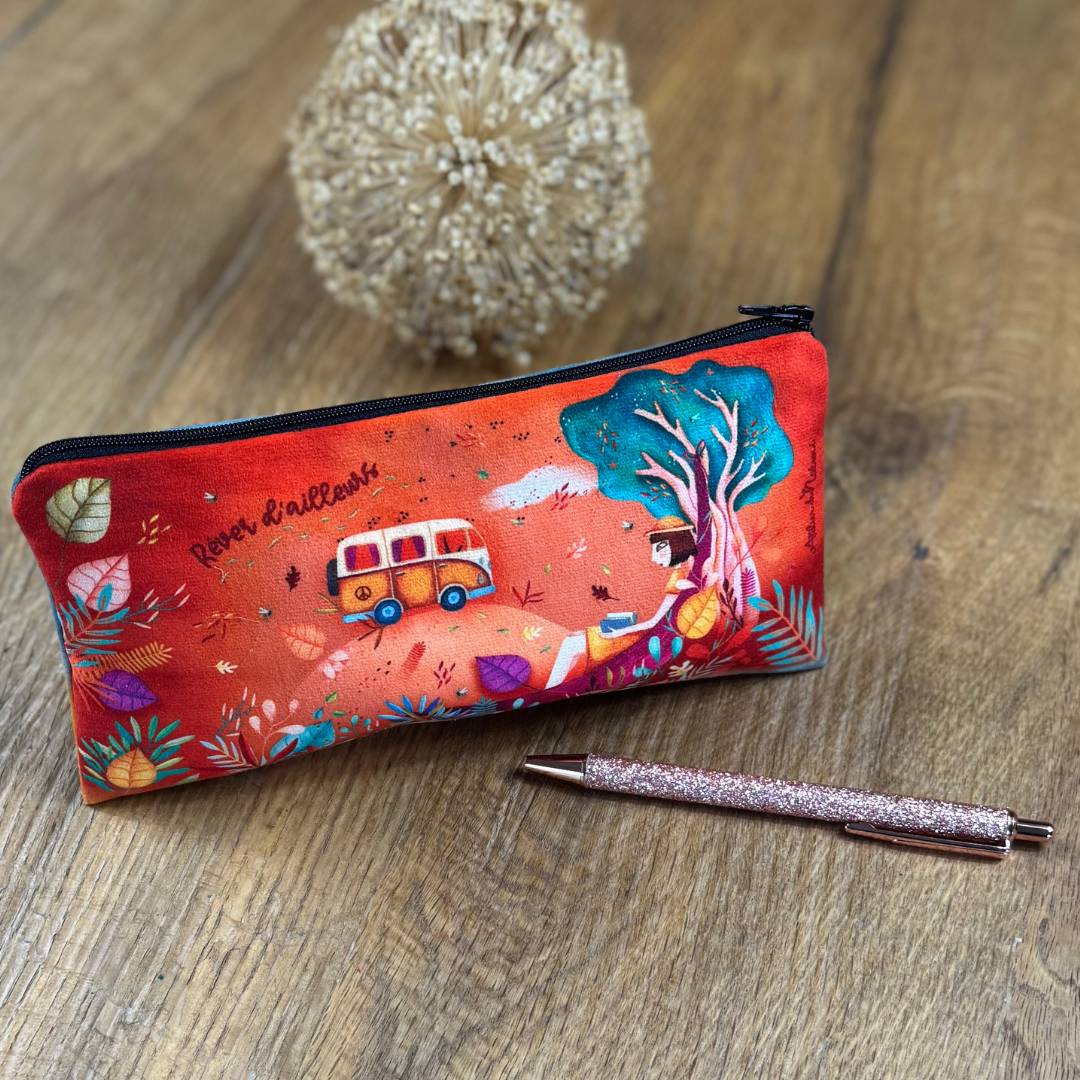 Federmäppchen Freiheit auf einen Holztisch, davor ein ein Stift, mit Motiv einer Frau in der Natur, dargestellt sind ein Bus und Bäume, die Hintergrundfarbe der Tasche ist orange