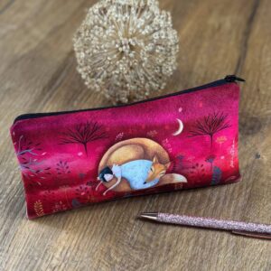 Federmäppchen Geborgenheit auf einem Holztisch mit Stift davor zeigt im Hintergrund einen Wald und davor eine Frau mit Fuchs