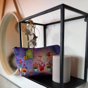 Schminktasche Blumenliebe auf einem Wandregal hinter einer Kerze, auf der Tasche sieht man Blumen, Fahrrad und leuchtende Farben