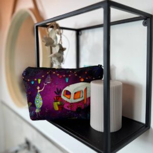 Schminktasche Lebensfreude auf einem Wandregel, davor eine Kerze mit farbigem Motiv, dargestellt ist eine Frau, ein Bus, Lichter und Pflanzen